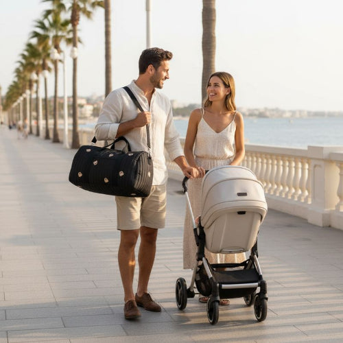 sac a langer noir papa avec le sac à l'épaule et maman avec la poussette au bord de la mer