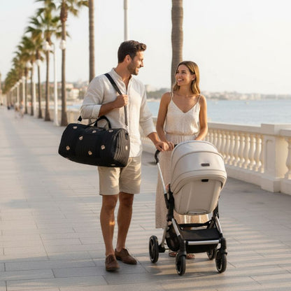 sac a langer noir papa avec le sac à l'épaule et maman avec la poussette au bord de la mer